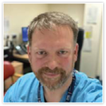 Headshot of Simon Watson, Medical Director and Director of Safety at HIS. He is wearing his blue hospital scrubs. 